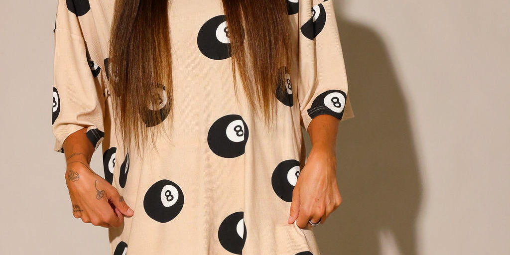 Model wearing a beige biker short, and short sleeve set with black 8 balls throughout, against a plain background, close up frontal view