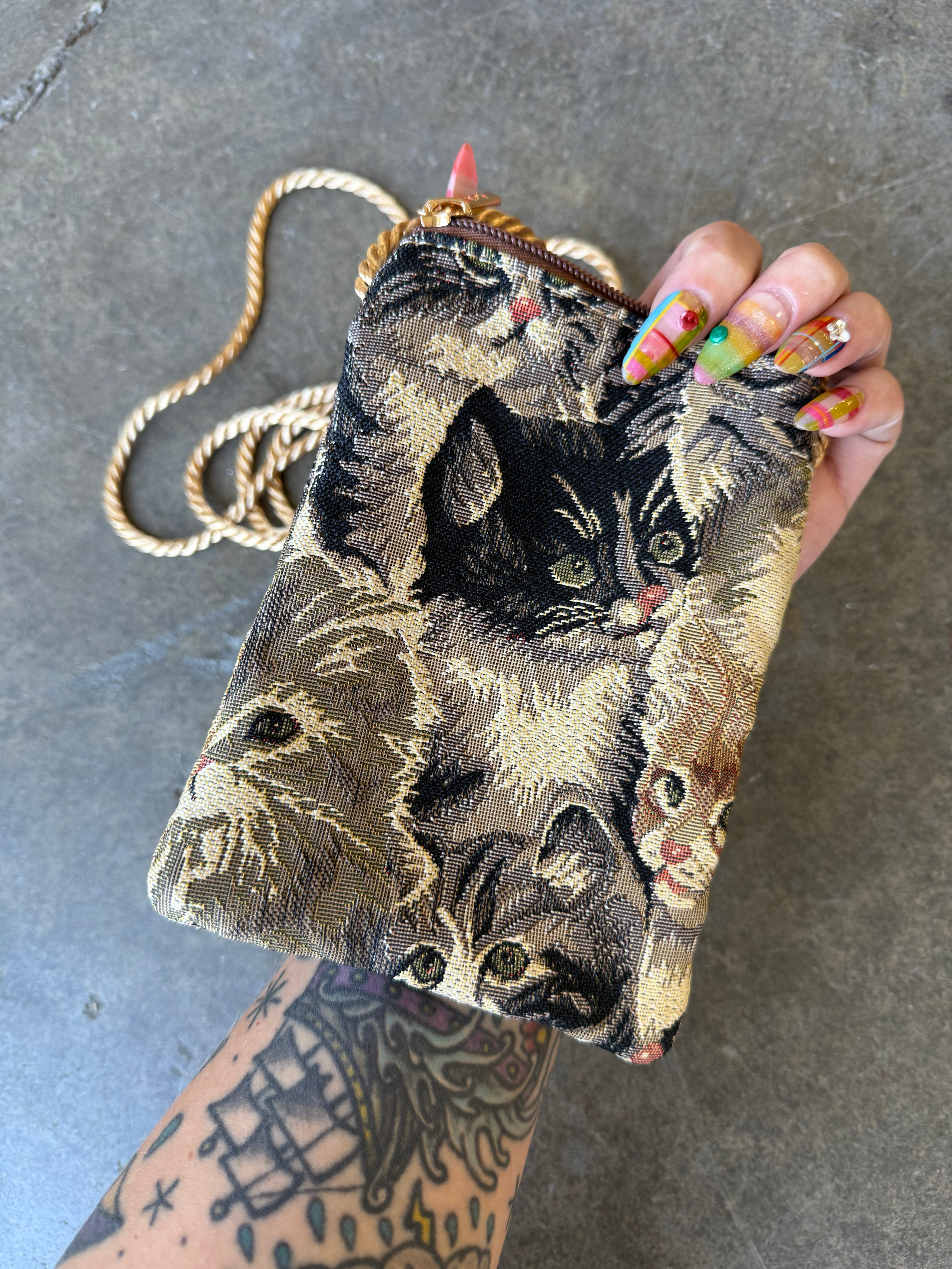 Hand holding a bag with a cat design and gold straps on a concrete background