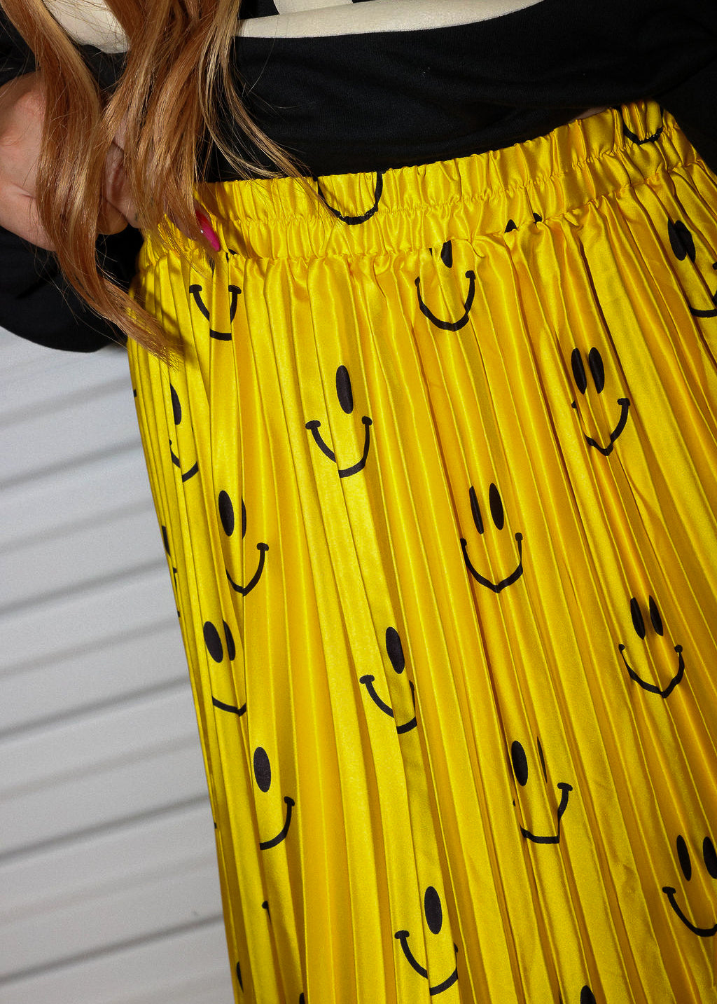 Yellow plisse skirt with smiley face pattern worn by a model, close up frontal view