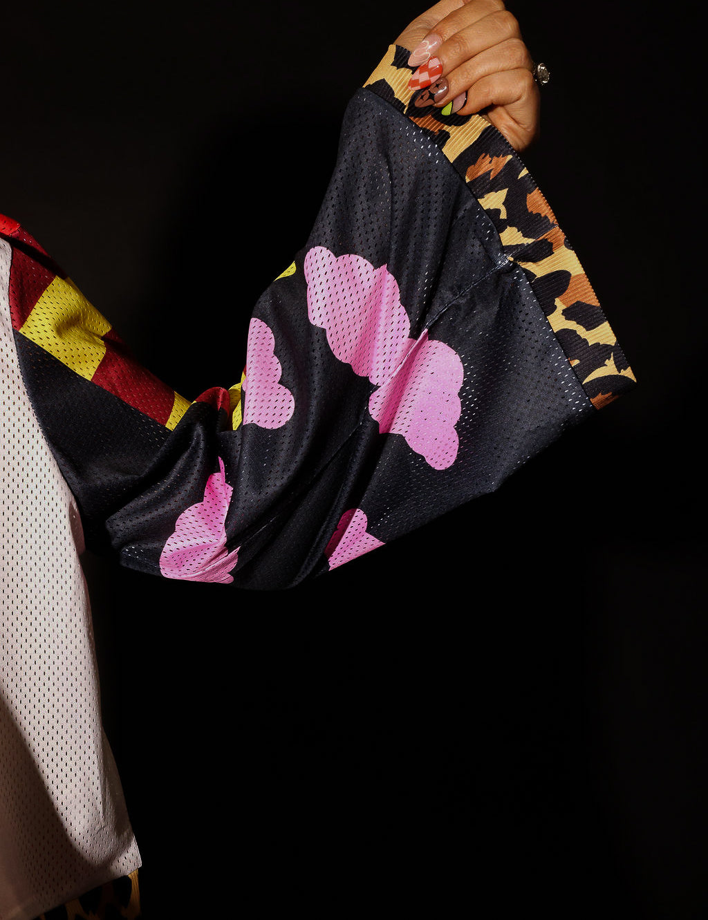 Close-up of a hand holding long sleeve a black fabric with pink cloud patterns against a dark background, close up frontal view