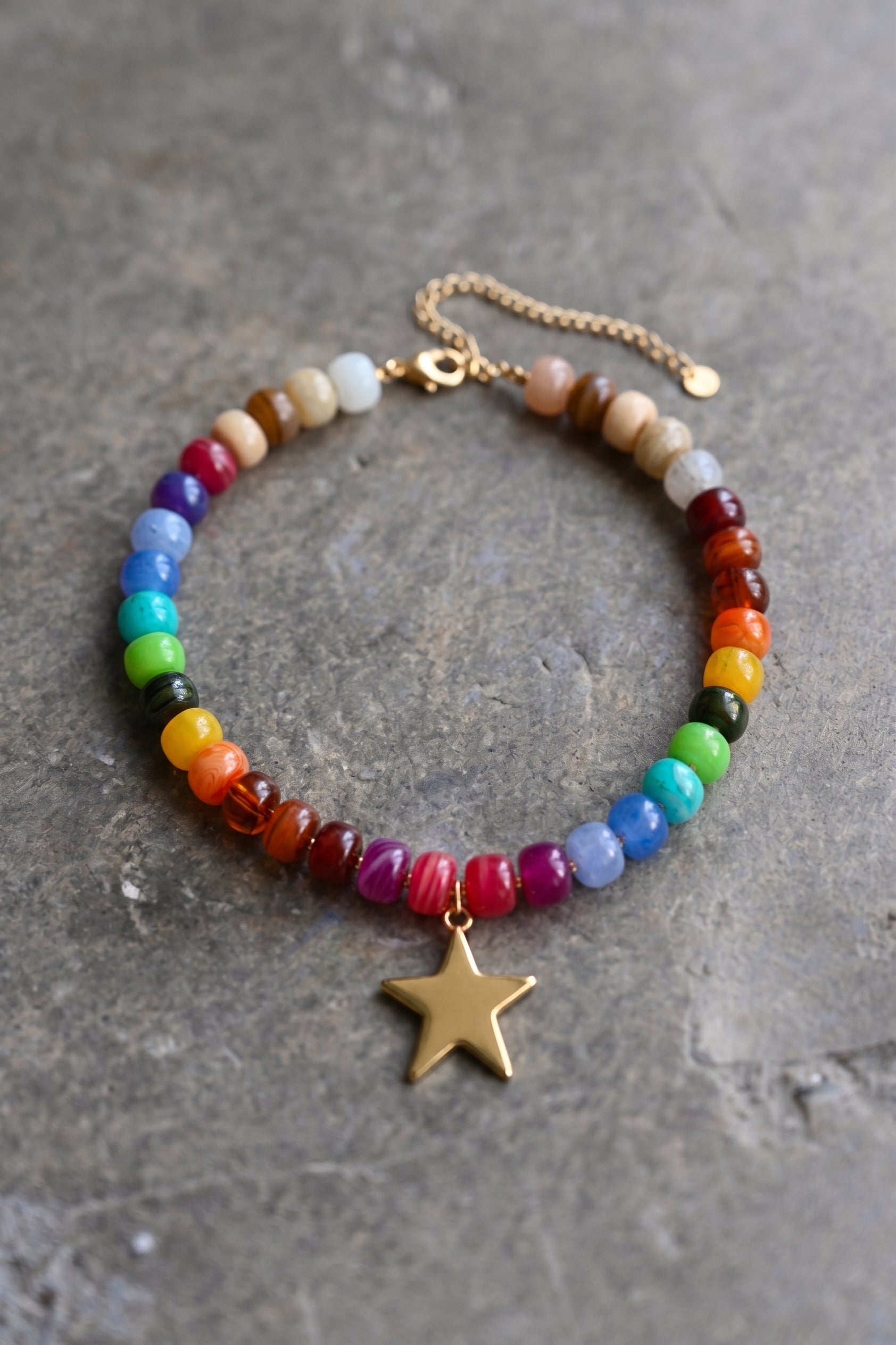 Rainbow beaded necklace, with gold star pendant on a grey textured surface