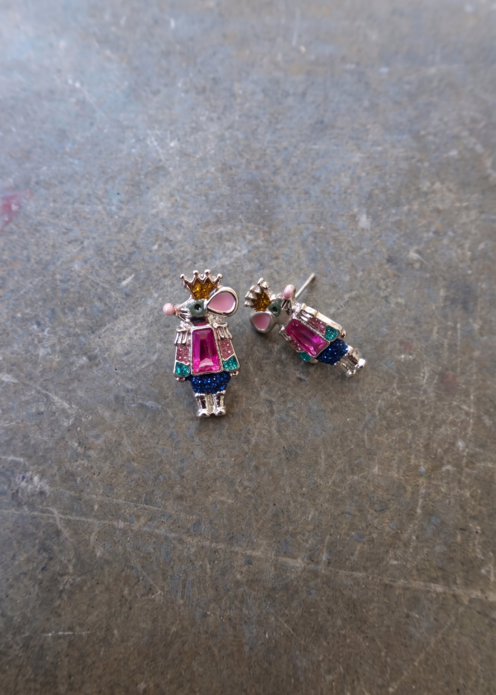 Silver earrings with pink and blue mouse figures with a gold crown on a dark surface