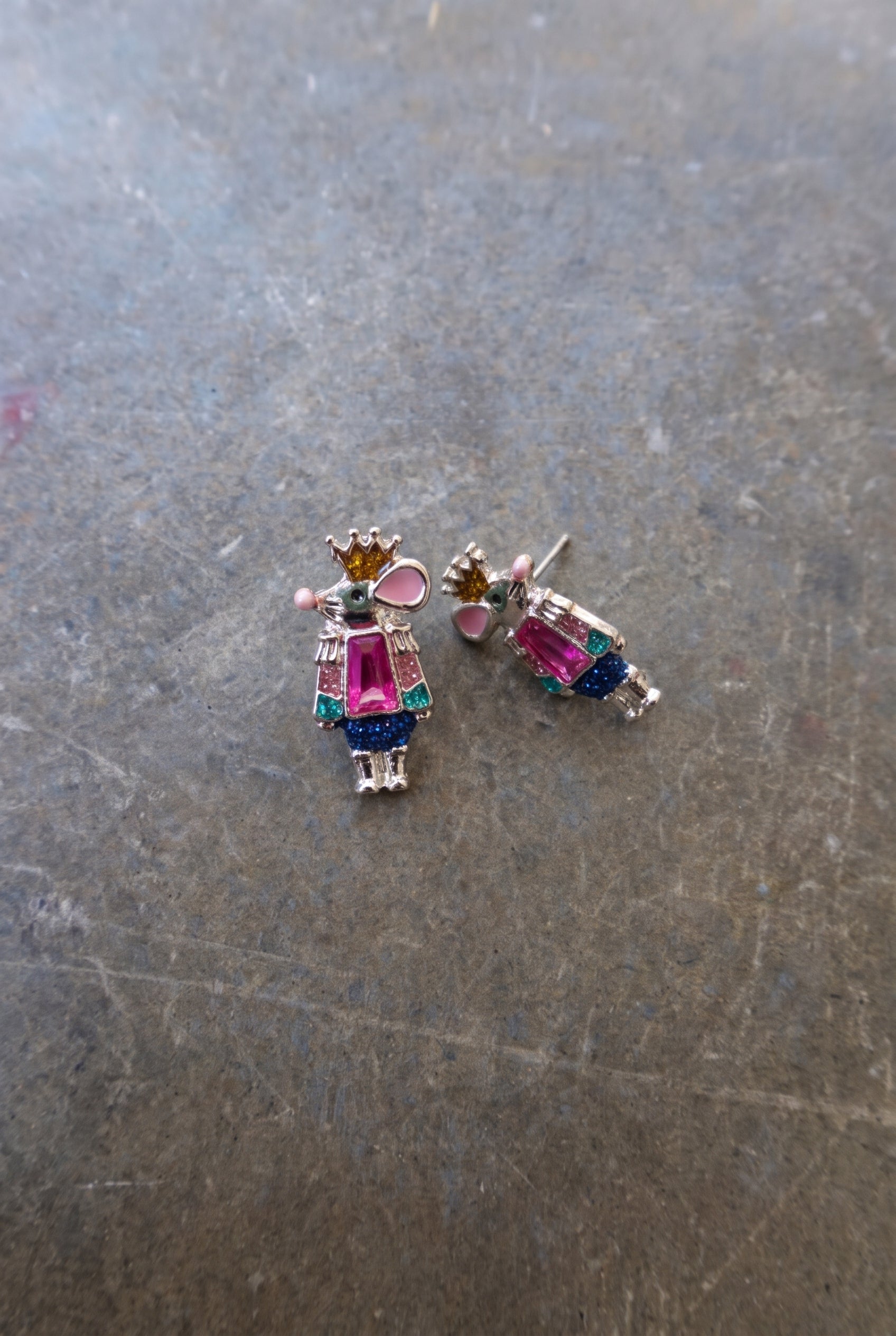Silver earrings with pink and blue mouse figures with a gold crown on a dark surface