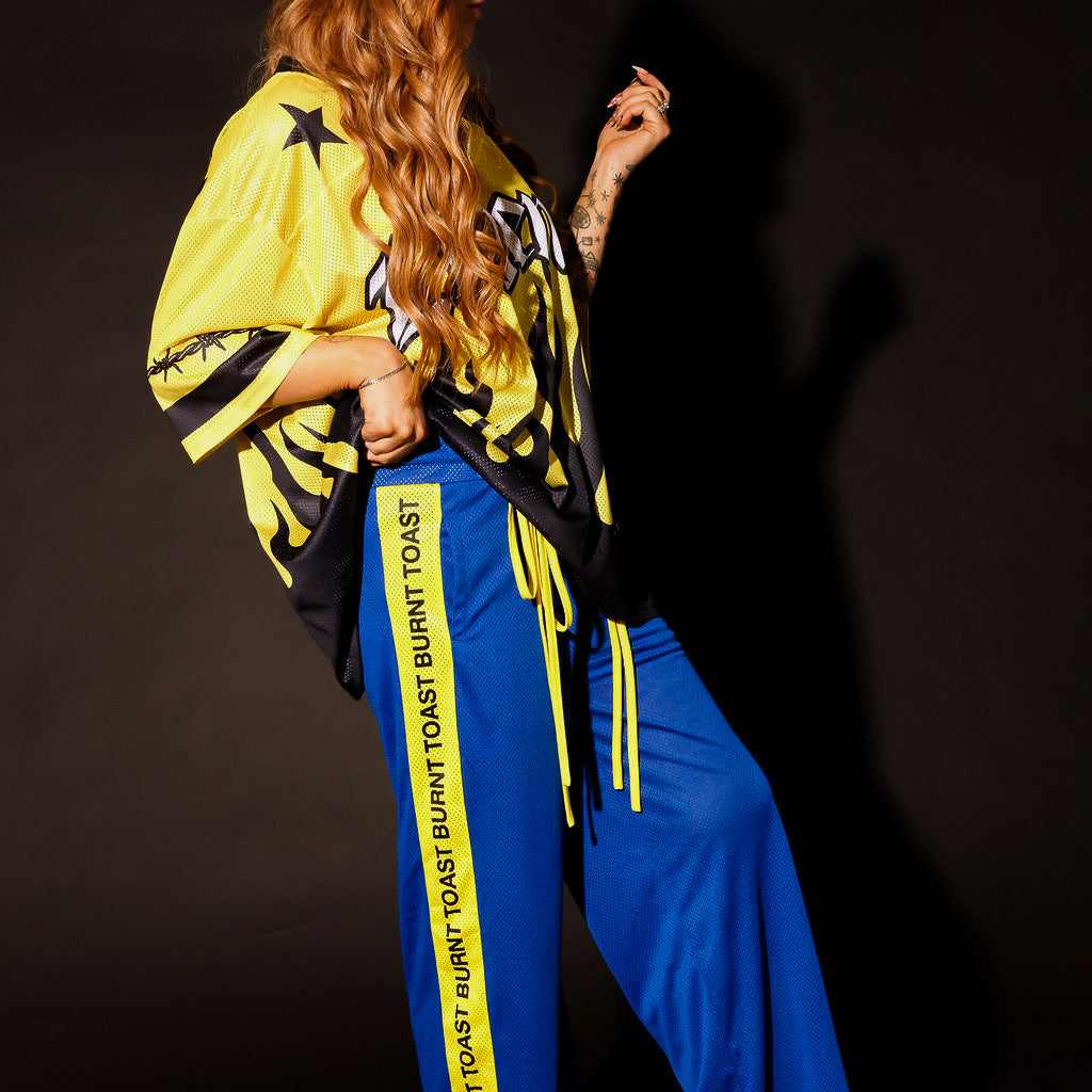 Model wearing a yellow and black short sleeve jersey and blue pants with yellow stripes against a dark background, side view