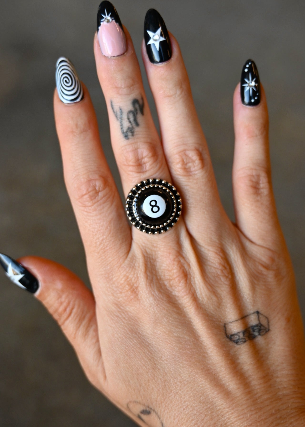 A hand wearing a silver ring with an 8 ball pendant on a dark background