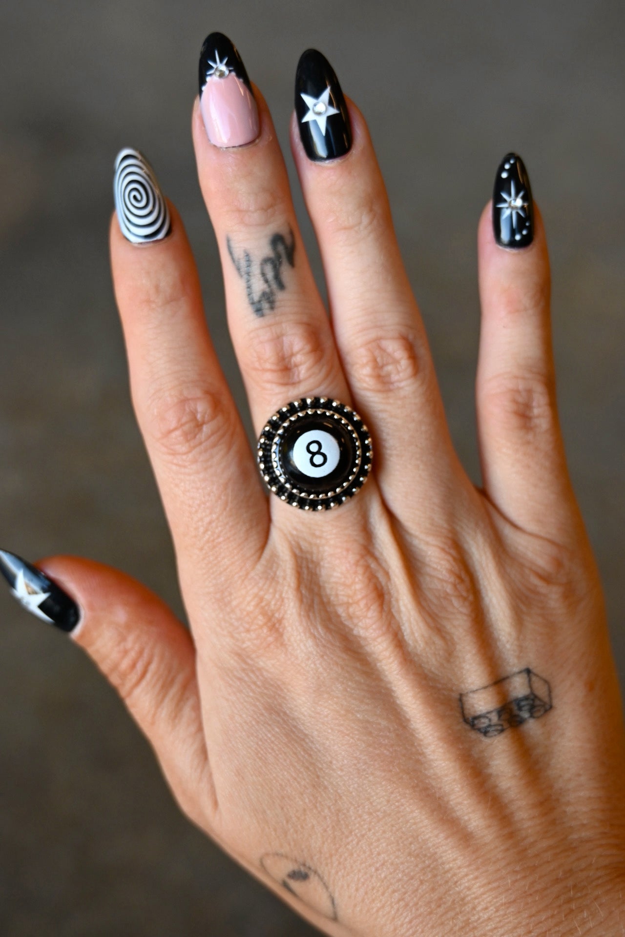 A hand wearing a silver ring with an 8 ball pendant on a dark background
