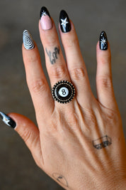 A hand wearing a silver ring with an 8 ball pendant on a dark background