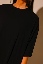 Close up of model wearing a black ribbed tee with a scoop neckline, showing the upper body and part of the shoulder