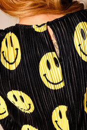 Model wearing a black short sleeve plisse top with yellow smiley face patterns, with clasp on neckline, close up back view