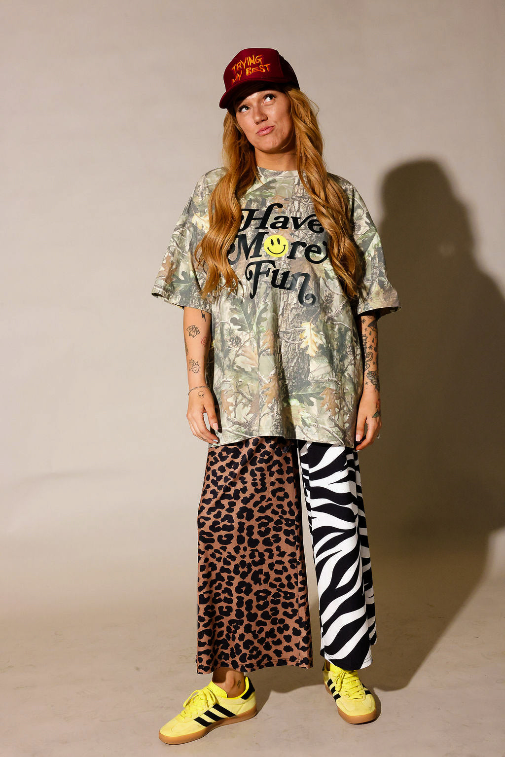 Model is wearing a camo graphic shirt, half leopard print pants, half zebra print pants on a beige background, frontal view