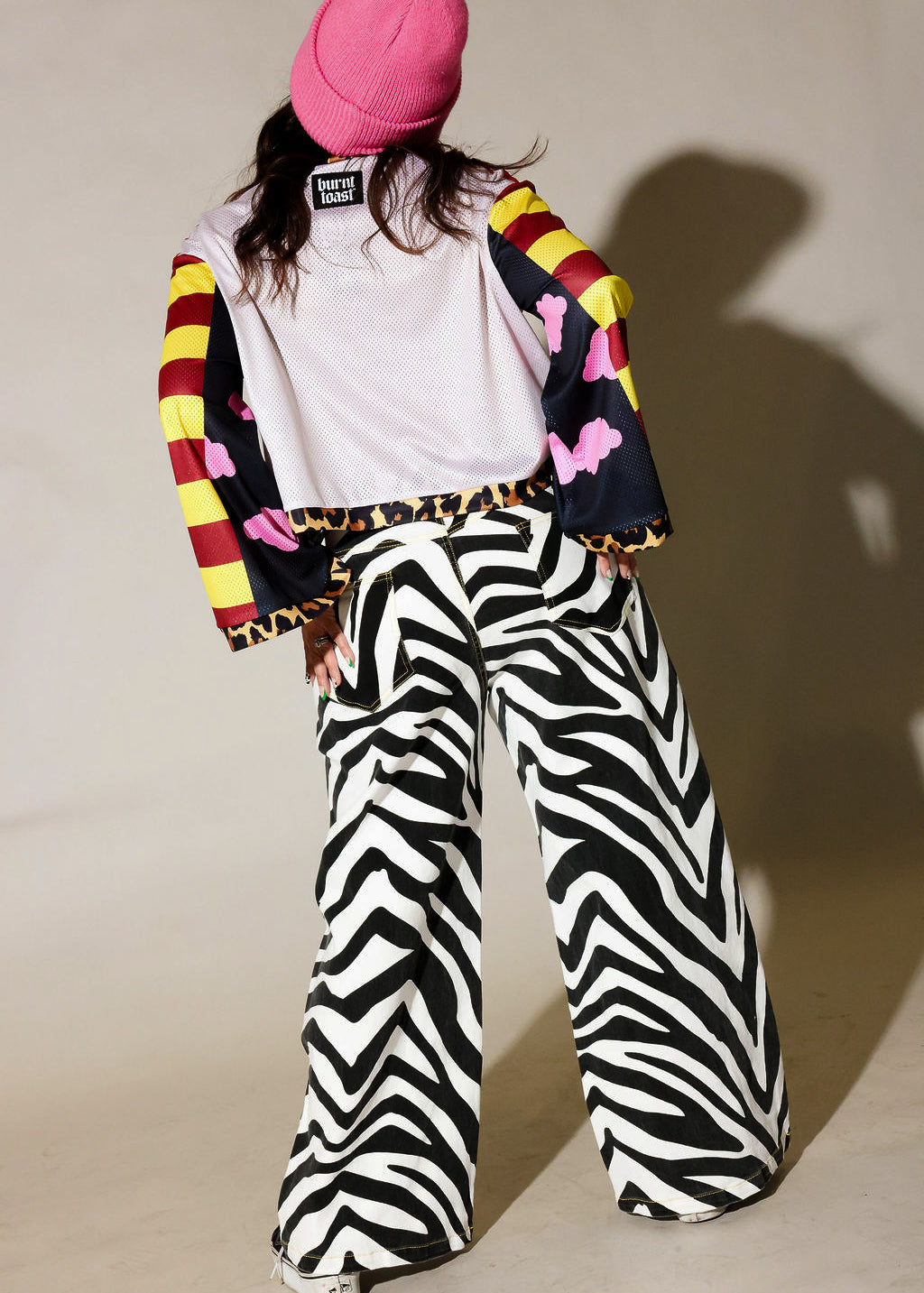 Person wearing a colorful jacket, white shirt, and zebra print pants against a plain background, back view