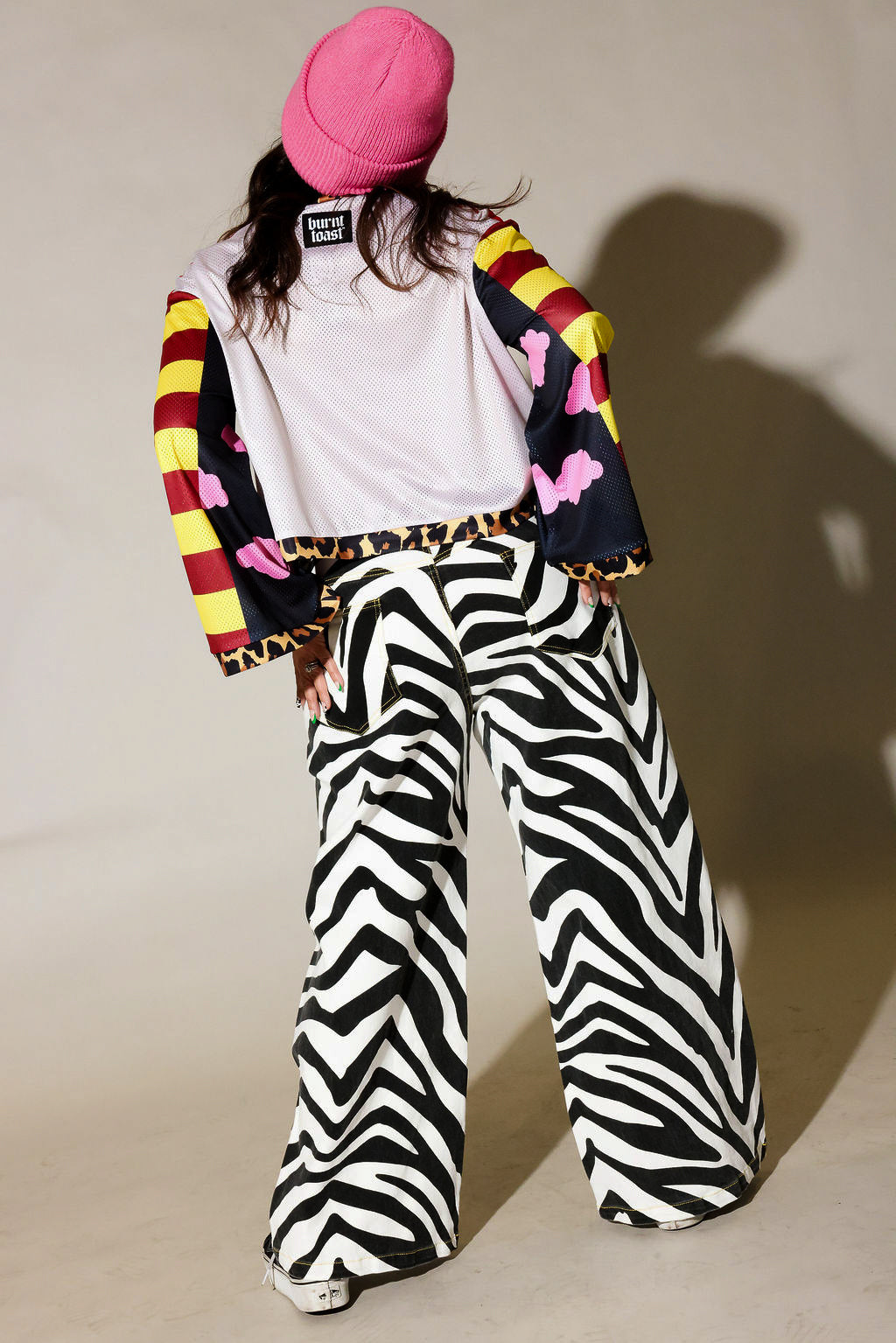 Person wearing a colorful jacket, white shirt, and zebra print pants against a plain background, back view