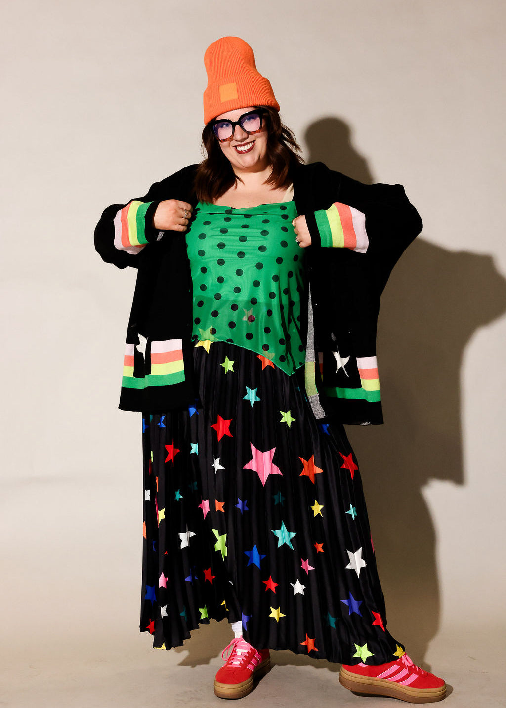 Person wearing a colorful outfit with a green top, black star-patterned skirt, and red shoes, frontal view