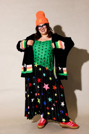 Person wearing a colorful outfit with a green top, black star-patterned skirt, and red shoes, frontal view
