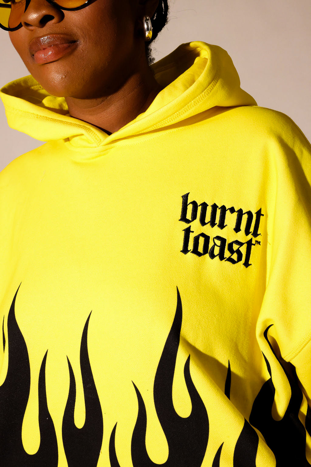 Model wearing a yellow hoodie with black flame and burnt toast logo, close up view