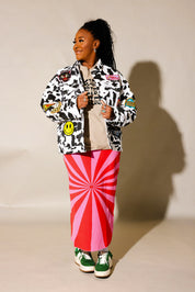 Model wearing a red and pink spiral patterned knit skirt, and cow pattern denim jacket, against a beige wall, frontal view