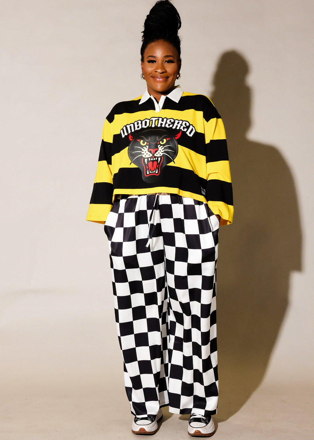 Model wearing a black and yellow striped polo, and black and white checkered pants, frontal view