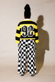 Model wearing a black and yellow striped polo with 92 on the back, and black and white checkered pants, back view
