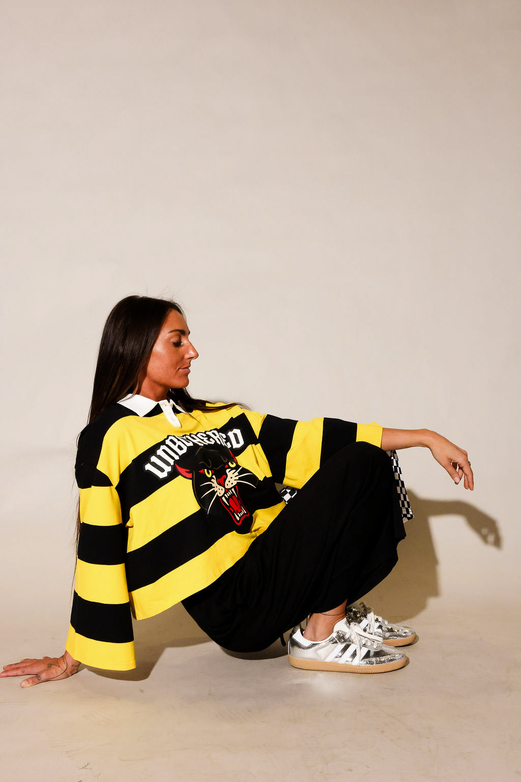 Model wearing a black and yellow striped polo with panther and 'UNBOTHERED' text, with black pants, on a beige background, side view