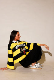Model wearing a black and yellow striped polo with panther and 'UNBOTHERED' text, with black pants, on a beige background, side view
