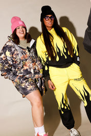 Two models posing in streetwear apparel. The model on the left wears a pink beanie and a camouflage-patterned hooded jacket and shorts set, frontal view