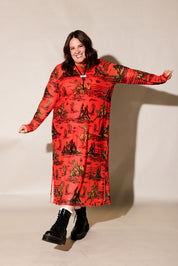 A woman modeling a long-sleeve red dress with a black and brown western-style print, paired with black boots, against a plain beige studio background, frontal view