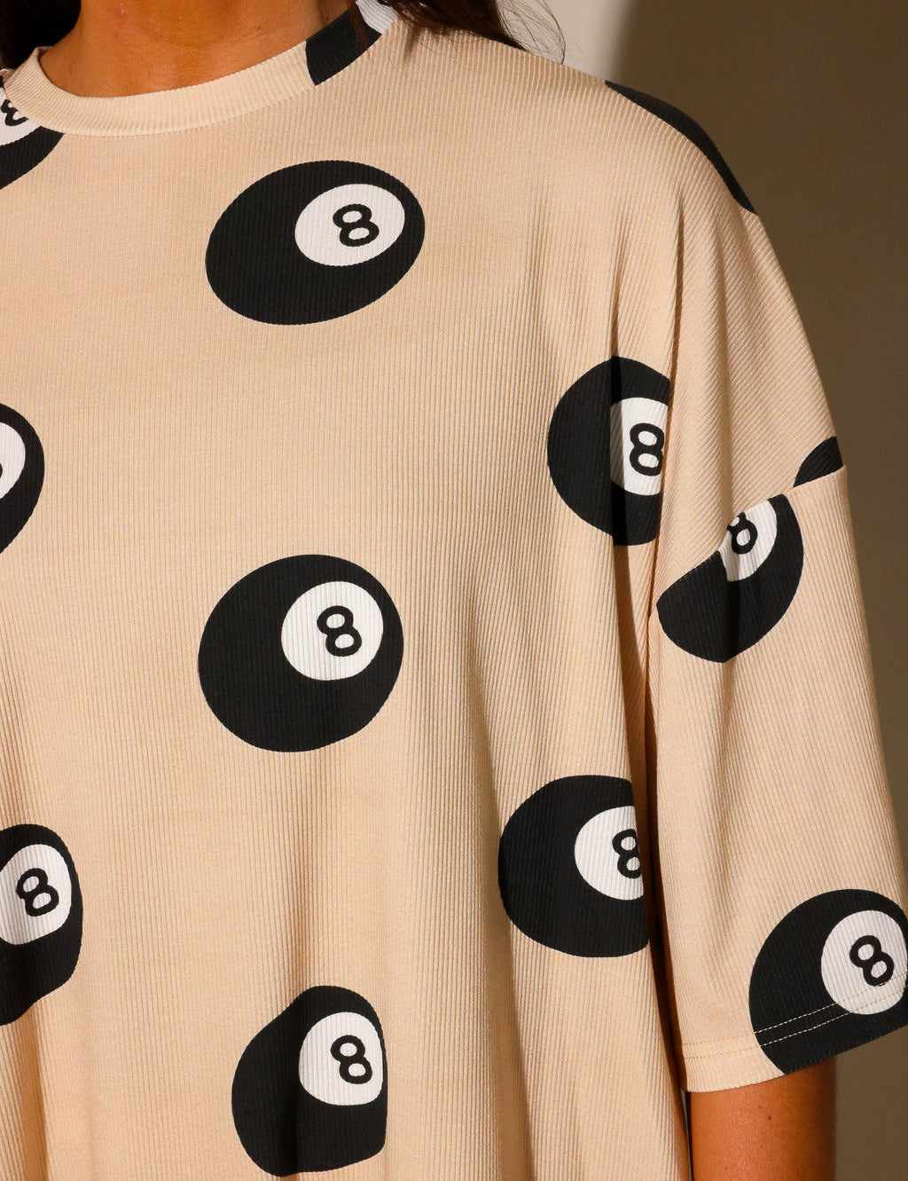Model wearing ribbed short sleeve shirt with black 8 balls throughout, against a plain background, highlighting collar, frontal view