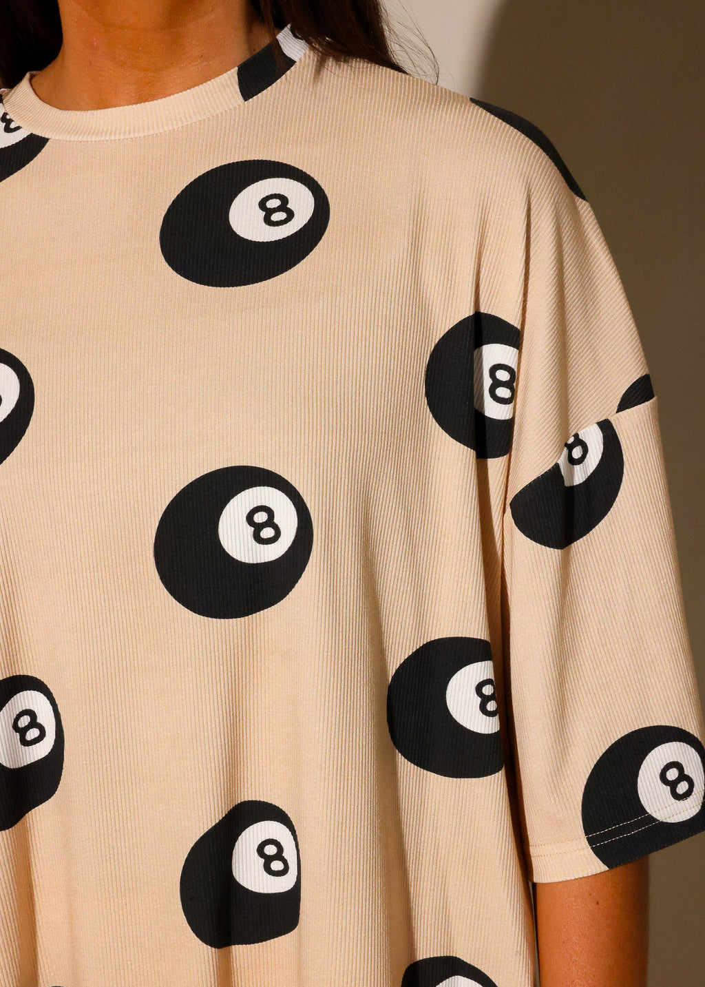 Model wearing ribbed short sleeve shirt with black 8 balls throughout, against a plain background, highlighting collar, frontal view