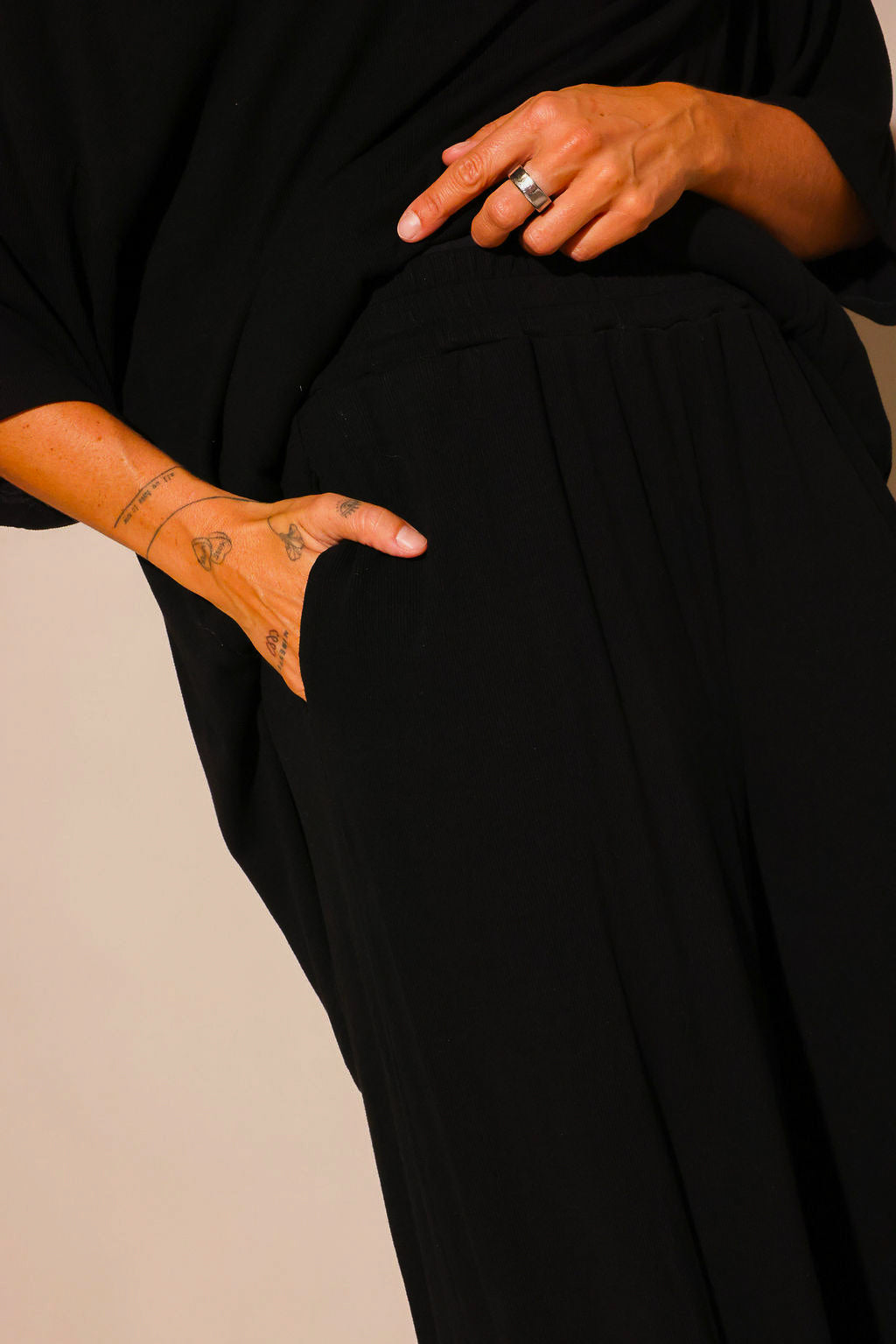 Close up of a model wearing a black ribbed two piece set, showing a hand in the pocket of the high waisted pants and the relaxed fit of the outfit
