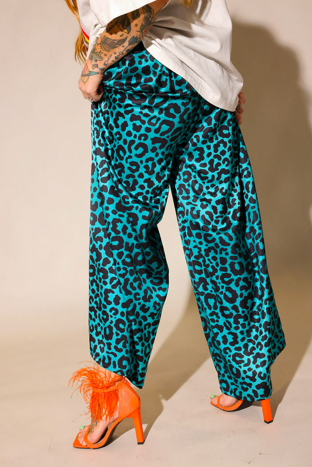 Model wearing teal and black leopard print pants worn by a person with orange shoes on a beige background, back view