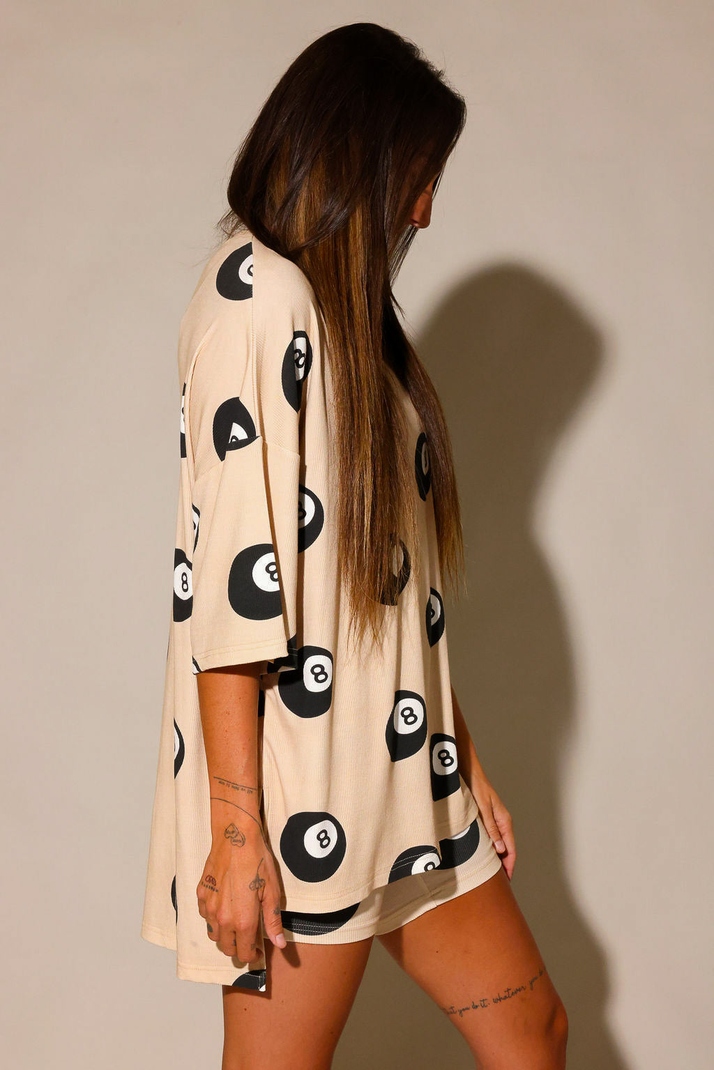 Model wearing a beige biker short, and short sleeve set with black 8 balls throughout, against a plain background, side view
