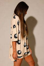 Model wearing a beige biker short, and short sleeve set with black 8 balls throughout, against a plain background, side view