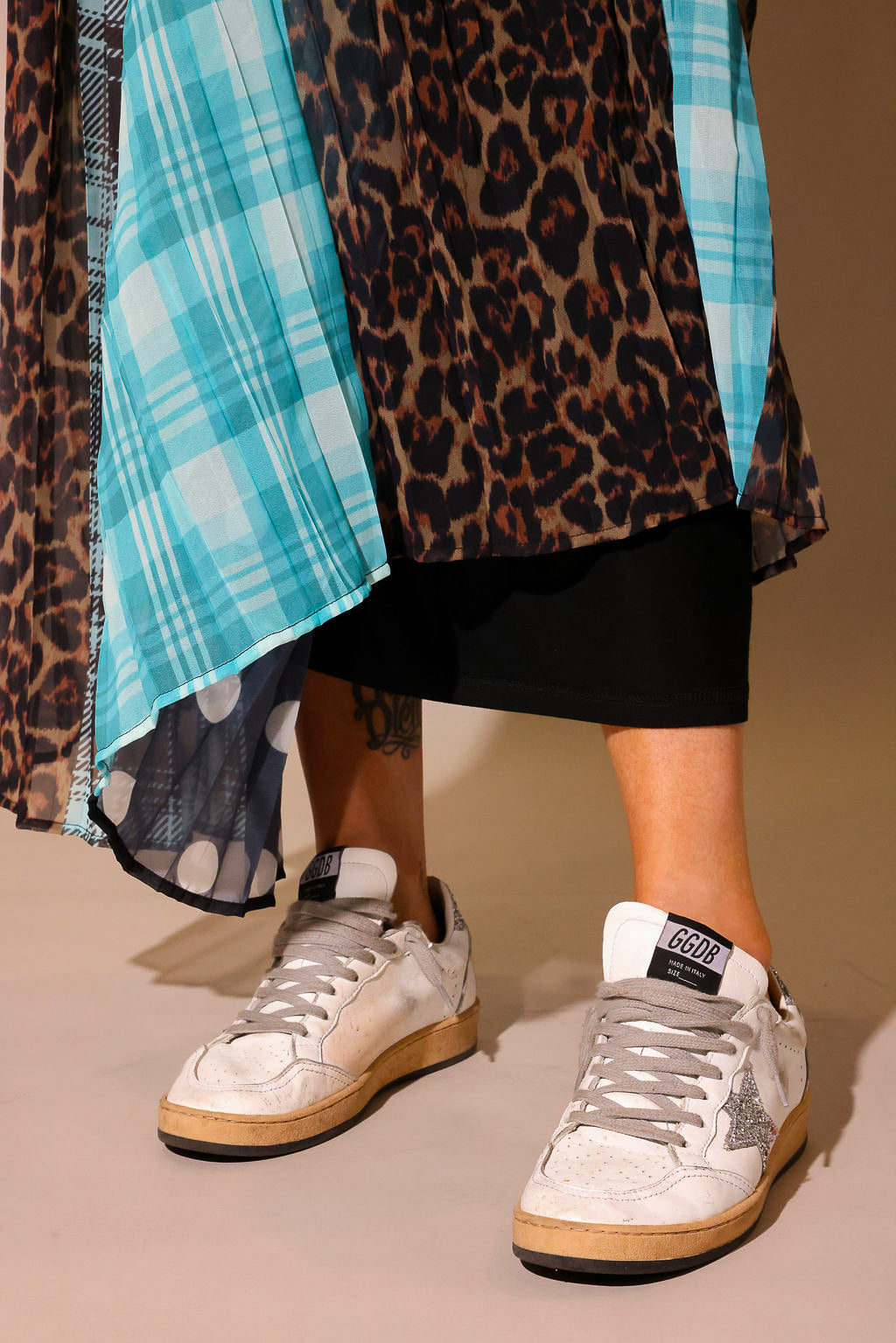 Model wearing a long, patterned skirt, with sections of black and white polka dots, blue flannel, brown flannel, and leopard prints, show the back slip underneath, against a plain background, lower half of body close up frontal view