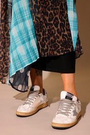Model wearing a long, patterned skirt, with sections of black and white polka dots, blue flannel, brown flannel, and leopard prints, show the back slip underneath, against a plain background, lower half of body close up frontal view