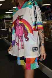Model wearing a colorful mesh short sleeve jersey with a unicorn and rainbow design, rainbow checkered pattern shorts, standing in an indoor setting. close up frontal view