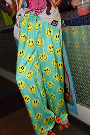 Model wearing seafoam green satin pants with yellow smiley face patterns, and roller skates, close up frontal view