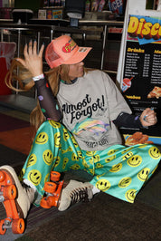Person sitting on a counter with roller skates, wearing colorful pants and graphic t-shirt