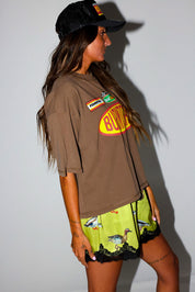 Woman wearing a brown t-shirt with a logo and satin shorts with lace trim and duck design, on a white background, side view