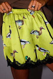 Model wearing green satin shorts with lace trim and duck design, frontal view
