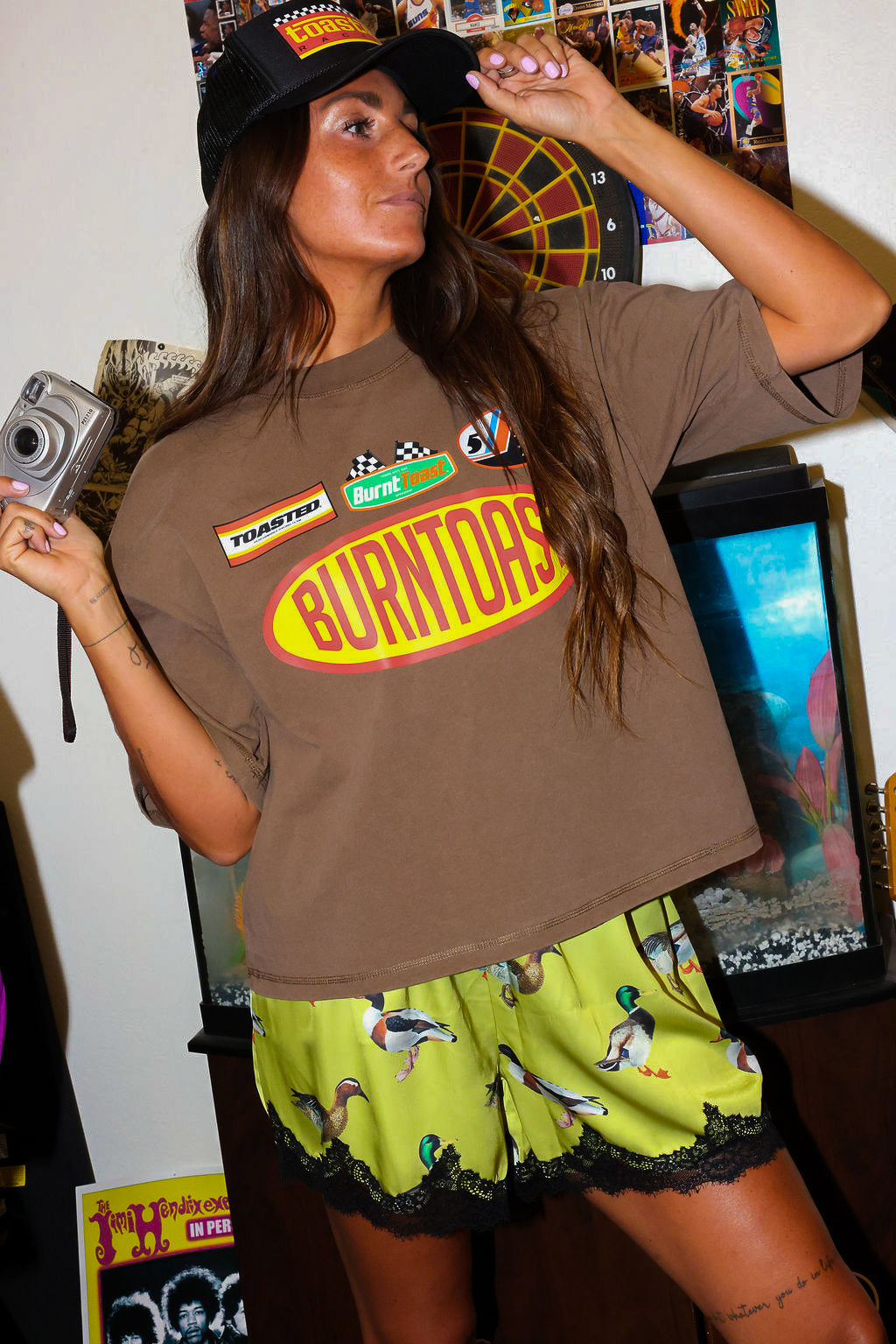 Woman wearing a brown t-shirt with a logo and satin shorts with lace trim and duck design, in a room, close up frontal view