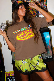 Woman wearing a brown t-shirt with a logo and satin shorts with lace trim and duck design, in a room, close up frontal view