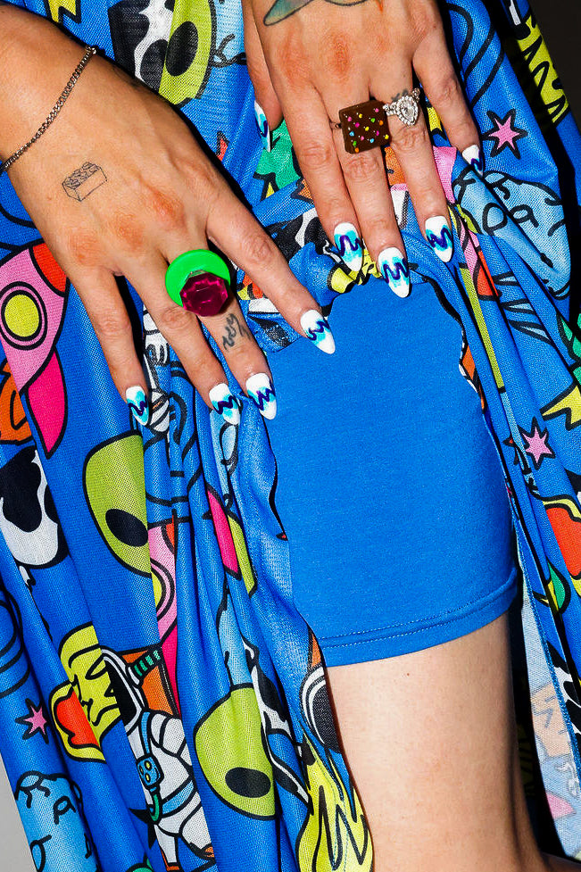 Close-up of hands with colorful nail art holding slip of dress, abstract background