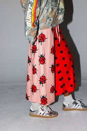 Model wearing a camo crewneck with Burnt Toast logo, red polka dot pants, and a yellow beanie, on a white background, side view