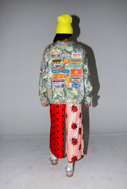 Model wearing a camo crewneck with logos, red polka dot pants, and a yellow beanie, on a white background, back view