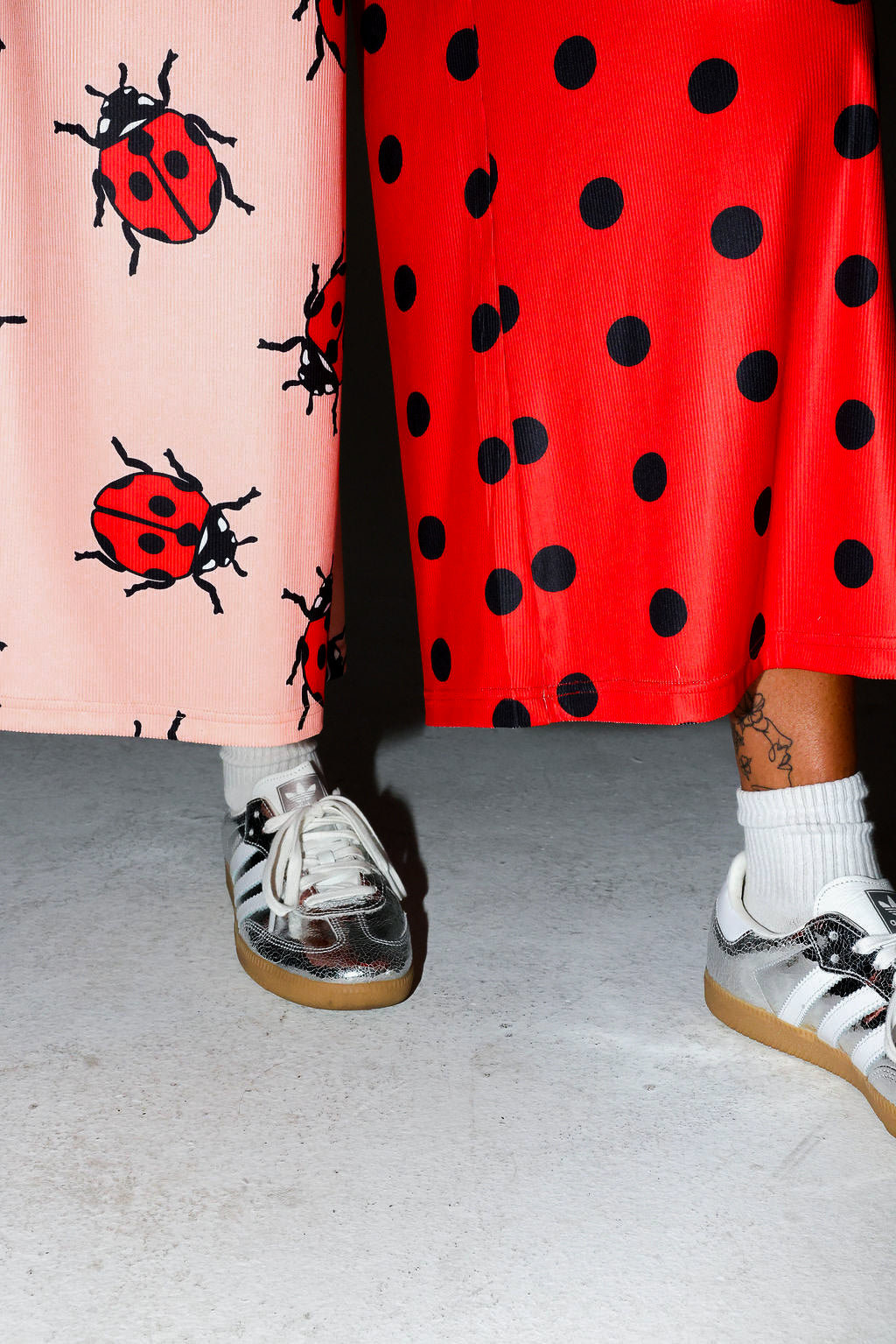 Model wearing red polka dot pants, and silver adidas, on a white background, close up frontal view