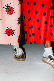 Model wearing red polka dot pants, and silver adidas, on a white background, close up frontal view