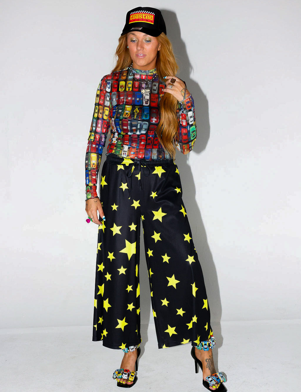 Model wearing a colorful patterned shirt and black pants with yellow stars on a white background, frontal view