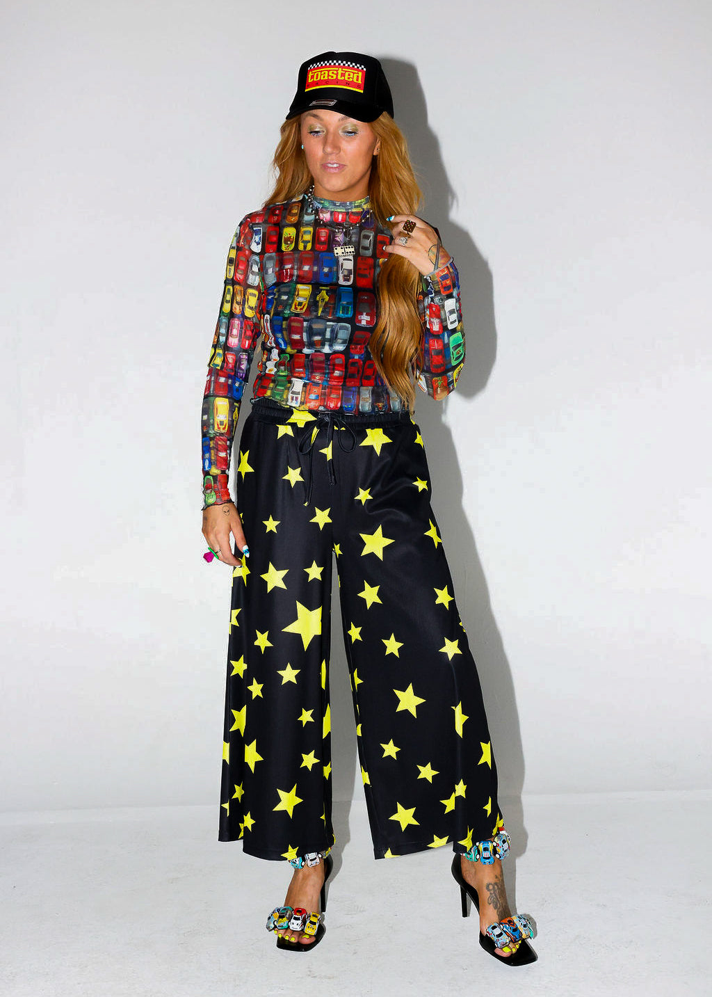 Model wearing a colorful patterned shirt and black pants with yellow stars on a white background, frontal view