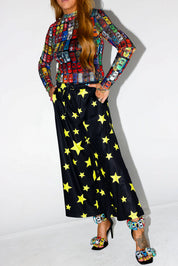 Model wearing a colorful long-sleeve shirt with toy car pattern and black pants with yellow stars, white background, close up frontal view