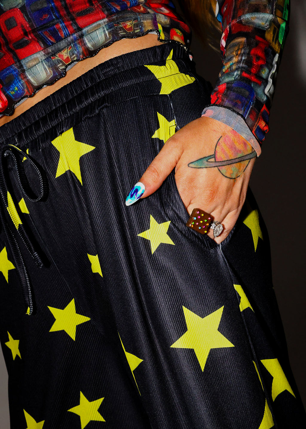 Model wearing black pants with yellow stars, colorful shirt, and hand in pocket, close up side view